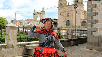 Jessica aus Chumbivilcas, Peru, steht vor einer historischen Kirche und zeigt stolz ihre Stärke, während sie traditionelle Kleidung trägt.