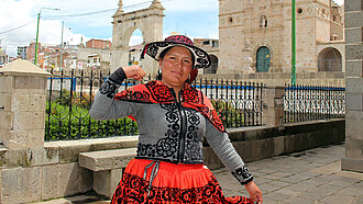 Jessica aus Chumbivilcas, Peru, steht vor einer historischen Kirche und zeigt stolz ihre Stärke, während sie traditionelle Kleidung trägt.