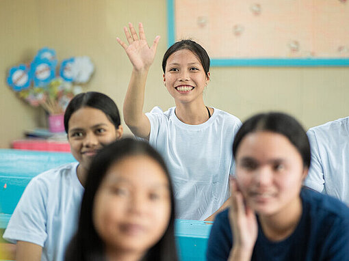 Eine Schülerin hält lächelnd eine Hand in die Luft für eine Wortmeldung