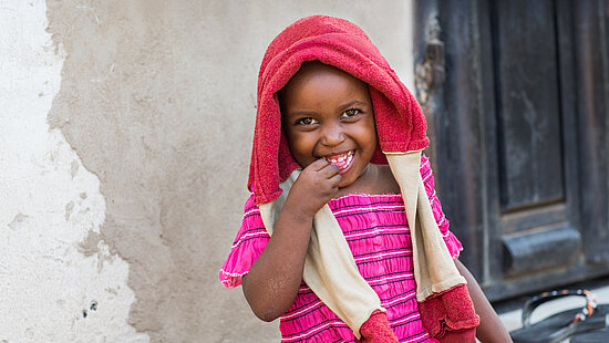 Ein kleines Kind sitzt lächelnd vor einem Hauseingang.