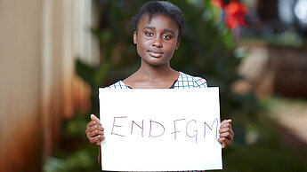 Plan-Hilfe in Deutschland: Projekt gegen FGM/C Eine junge Frau aus Kenia hält ein weißes Schild hoch, auf dem "END FGM" steht