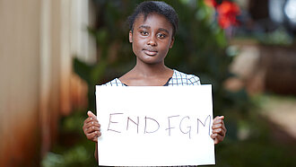 Eine junge Frau aus Kenia hält ein weißes Schild hoch, auf dem "END FGM" steht