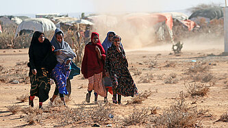 Eine Gruppe somalischer Mädchen laufen über staubtrockene Erde durch ein Camp für Binnengeflüchtete