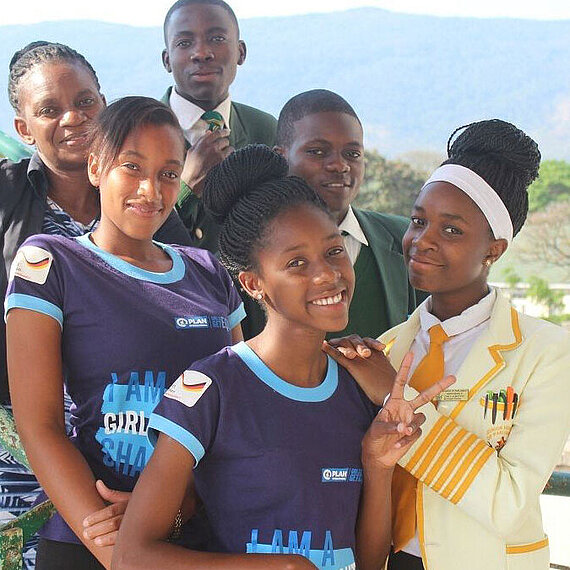 Eine Gruppe junger Jungen und Mädchen tragen T-Shirts von Plan International und gucken glücklich in die Kamera.