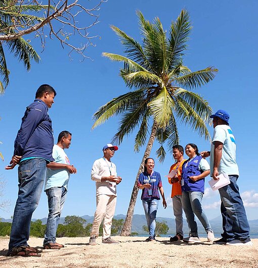 Eine Gruppe von Frauen und Männern steht im Halbkreis an einem Strand