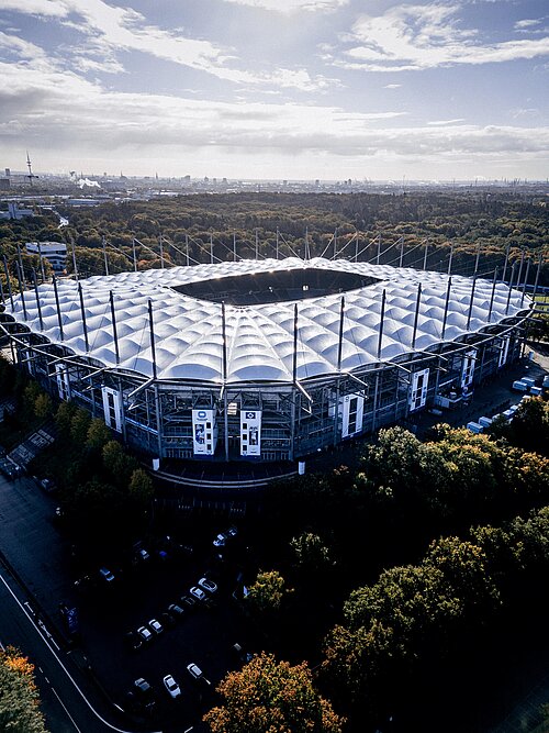 Im Vordergrund ist das Volksparkstadion, Heimspielstätte des HSV, in stimmungsvollem Licht.