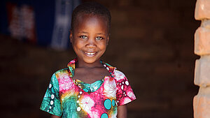 Ein Mädchen mit geblümten Kleid lächelt in die Kamera.