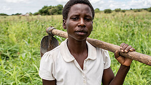 Jugendliche Bäuerin in Sambia mit Hacke – Alltag auf dem Land Jugendliche Bäuerin in Sambia steht mit Hacke auf der Schulter auf einem Feld – Symbol für harte Arbeit und Lebensrealität ländlicher Mädchen.