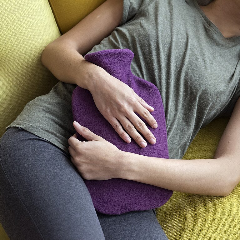 Eine Frau liegt mit einer Wärmflasche auf dem Bauch auf einem Sofa