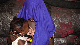 Fatoumata trägt ein Tuch über dem Kopf, sodass man ihr Gesicht nicht erkennen kann. Sie hält ihre kleine Tochter im Arm