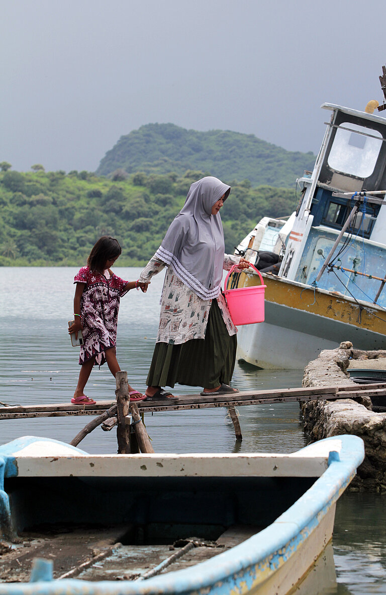 Eine Frau und eine Kind laufen über eine Planke zwischen Booten.