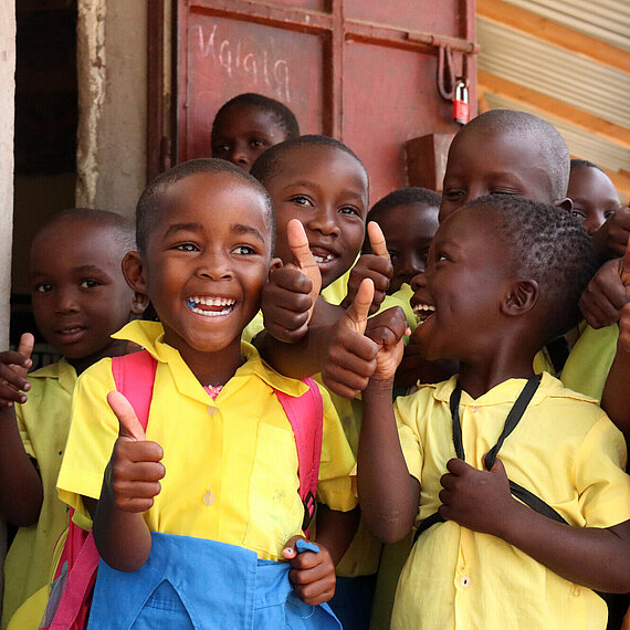 Kinder in Kenia freuen sich über ihren Schulbesuch und zeigen Zusammenhalt Fröhliche Grundschulkinder in Kenia zeigen Daumen hoch und lachen in die Kamera