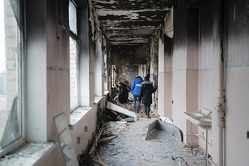 Drei Menschen gehen durch einen durch eine Explosion zerstörten Schulflur