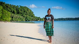 Jayleen steht am Strand ihres Zuhauses auf Nggatokae