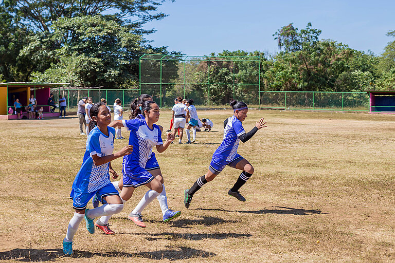 Drei Mädchen in blauen Fußball-Trikots sprinten über ein Feld.