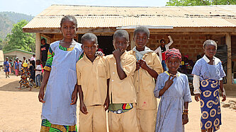 Sechs Kinder, die in die ernst Kamera schauen, vor ihrem alten, baufälligen Schulgebäude