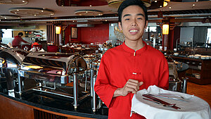 Gastronomie-Ausbildung: Service im Restaurant in Vietnam Junger Kellner in roter Kleidung mit Besteck vor einem Buffet in einem Restaurant in Vietnam.