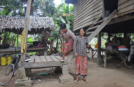 Muon und Ming stehen neben einer Holzhütte auf Stelzen.
