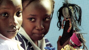 Mädchen aus Mali präsentieren ihre selbst gebastelten Puppen aus Stoffresten und Blättern.