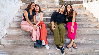 Vier junge Frauen sitzen auf einer Treppe zusammen und lächeln in die Kamera