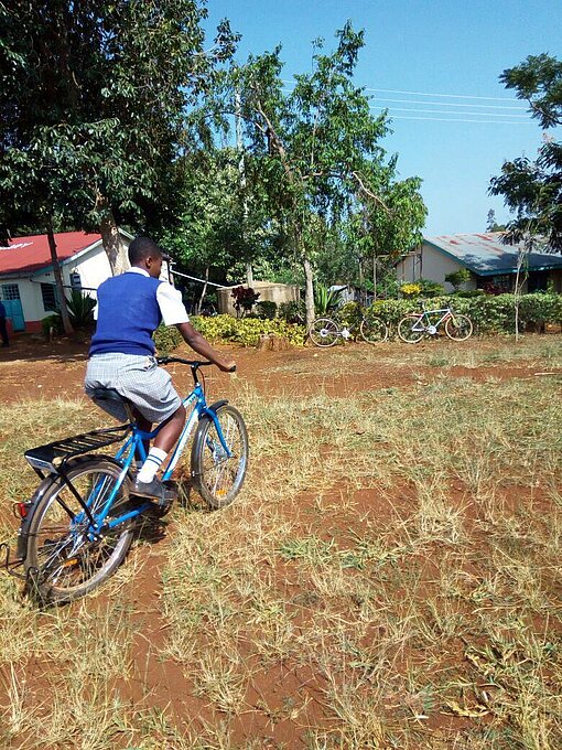 Magdaline fährt mit dem Fahrrad über einen Acker.