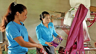 Zwei Frauen beugen sich über gewebten Stoff