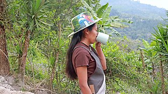 Eine junge Frau steht an einem Waldrand und trink aus einem Becher