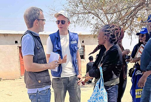 Mehrere Personen stehen vor einem Gebäude aus Lehm