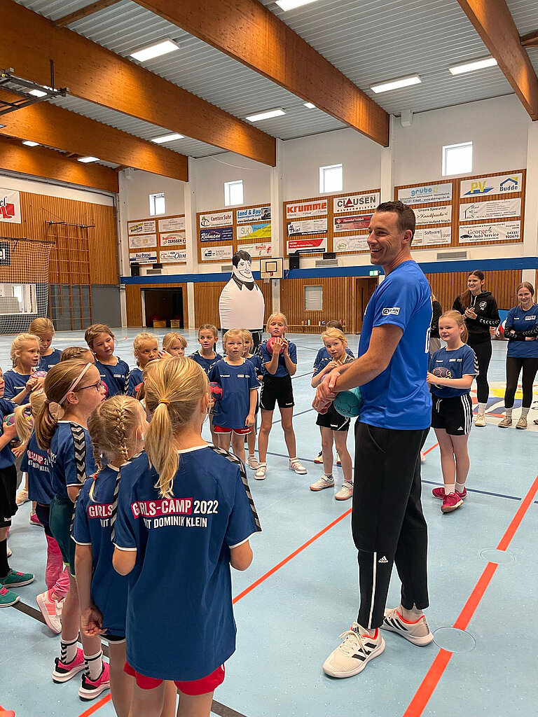Dominik Klein steht vor einer Gruppe Mädchen in Handball Trikots.