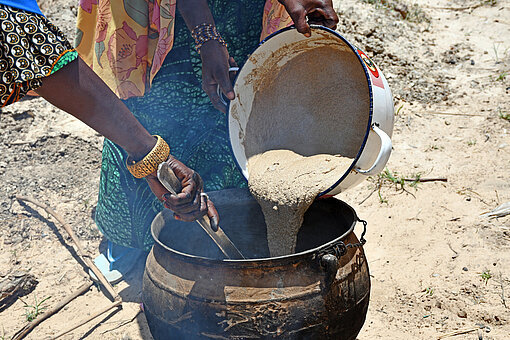 Nahaufnahme auf einen großen Topf, in den mit einem kleineren Topf Porridge gefüllt wird.