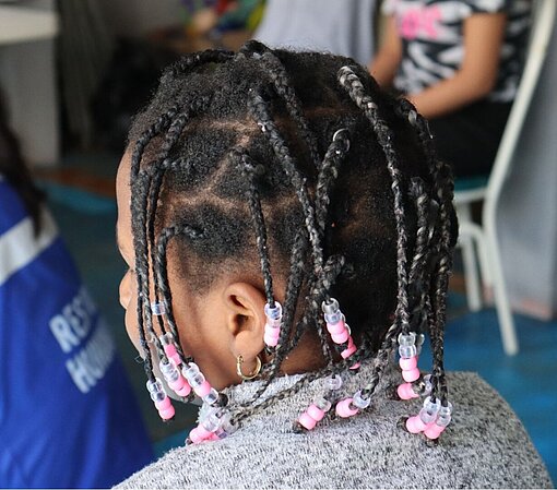 Auch dieses Mädchen wartet in einer Sammelunterkunft darauf, endlich in die USA einreisen zu dürfen Hinterkopf eines Mädchen mit Dreadlocks und bunten Perlen im Haar