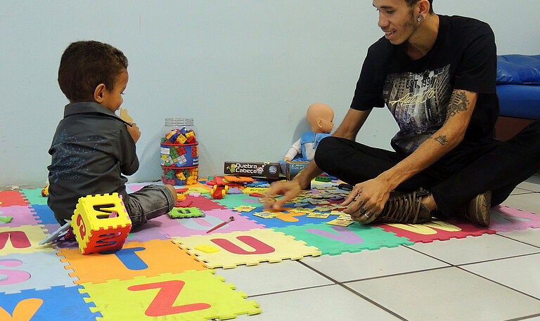 Valnei spielt mit seinem Kind auf Buchstabenteppich.
