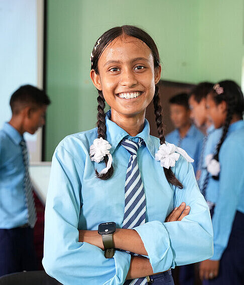 Mädchen in Schuluniform lächelt mit verschränkten Armen in die Kamera
