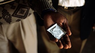 Ein verpacktes Kondom liegt auf der ausgestreckten Handfläche eines Mannes 