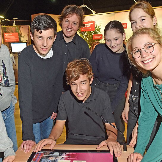 Mädchen und Jungen beugen sich über einen Tisch mit einer interaktiven Lernaufgabe