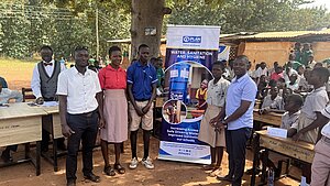Schülerinnen, Schüler und Lehrkräfte stehen neben einem Plan-International-Banner zu Wasser, Sanitärversorgung und Hygiene in einer Schule.