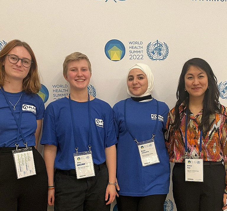 Vier junge Menschen stehen in Plan T-Shirts vor der Pressewand der Weltgesundheitskonferenz