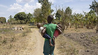 Nalongo geht in ihrer Gemeinde und trägt ihre Kinder in den Armen