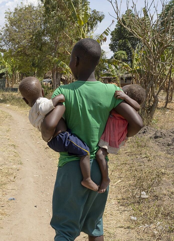 Nalongo geht in ihrer Gemeinde und trägt ihre Kinder in den Armen