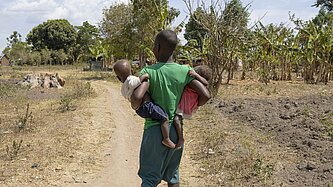 Nalongo geht in ihrer Gemeinde und trägt ihre Kinder in den Armen