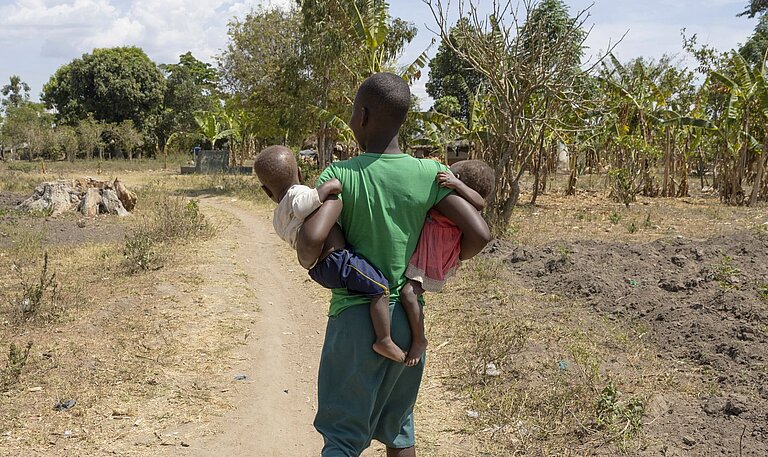 Nalongo geht in ihrer Gemeinde und trägt ihre Kinder in den Armen