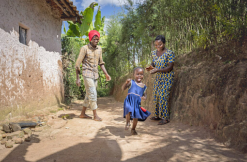 Ein kleines Mädchen spielt lachend und ihre Eltern schauen zu