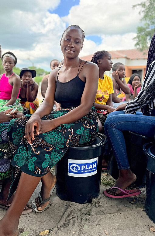 Eine Frau sitzt auf einem Eimer mit dem Logo von Plan International