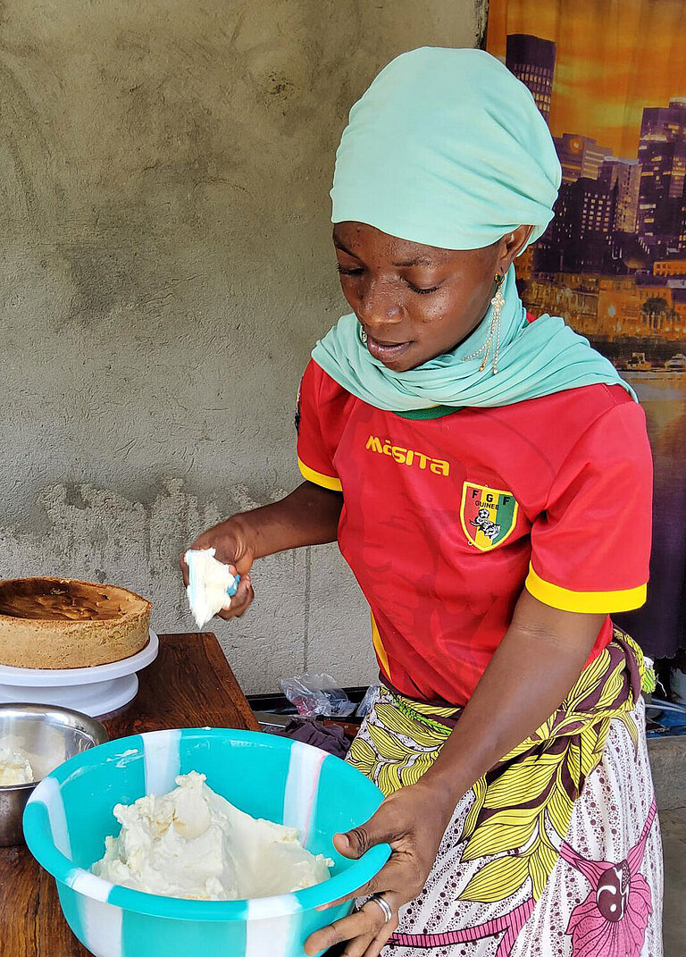 Eine junge Frau hält eine Schüssel in der Hand und fügt etwas hinein, um Kuchenglasur herzustellen