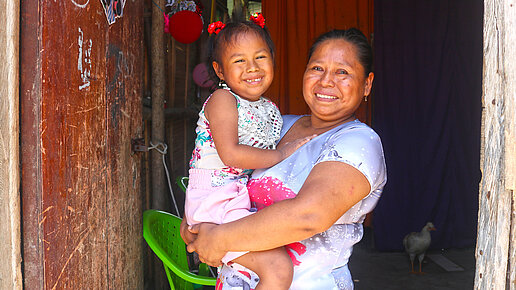Eine Mutter hält lächelnd ihre kleine Tochter auf dem Arm.