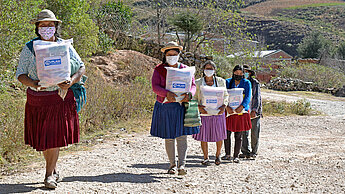 Frauen tragen Corona-Nothilfepakete in einer bolivianischen Gemeinde nach Hause. Diese enthalten neben Lebensmitteln auch notwendige Hygieneartikel. ©Plan International