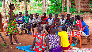 Jugendliche sitzen in einem Kreis und nehmen an einem Bildungsworkshop im Freien in einem Dorf in Uganda teil