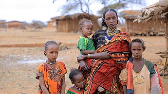 Eine äthiopische Frau steht draußen und hält ein Kleinkind im Arm, um sie herum stehen drei weitere Kinder