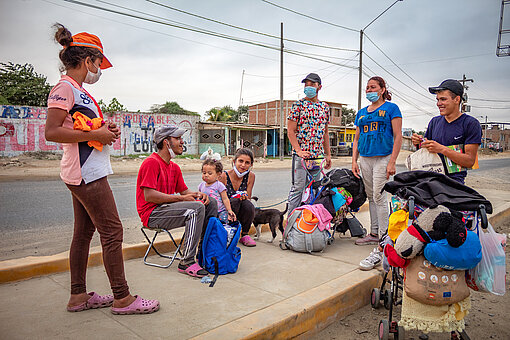 Eine Gruppe geflüchteter Menschen steht und sitzt an einer Straße und unterhält sich.
