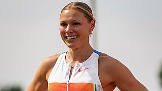 Porträt einer sportlich gekleideten Frau mit zurückgebundenen Haaren, die lächelt und ein ärmelloses Sportoberteil trägt. Der Hintergrund ist hell und unscharf.